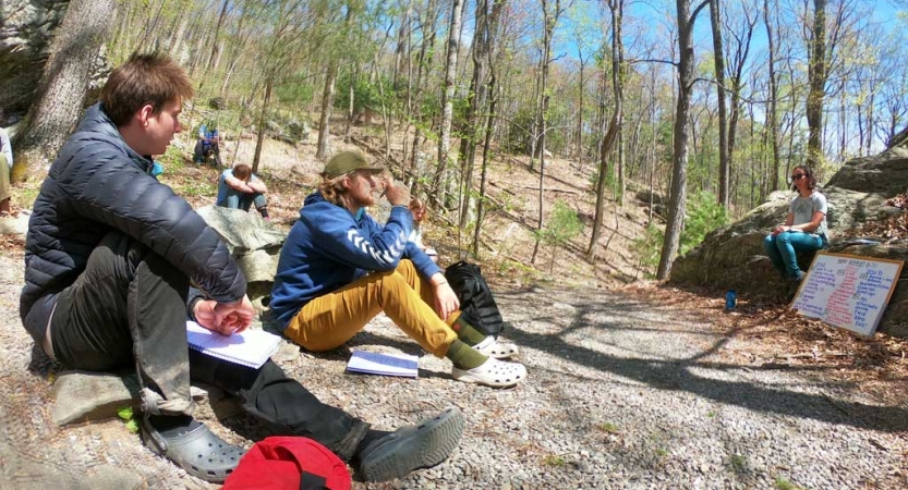A group of people sit on the ground and listen to an instructor during a WFR course. 
